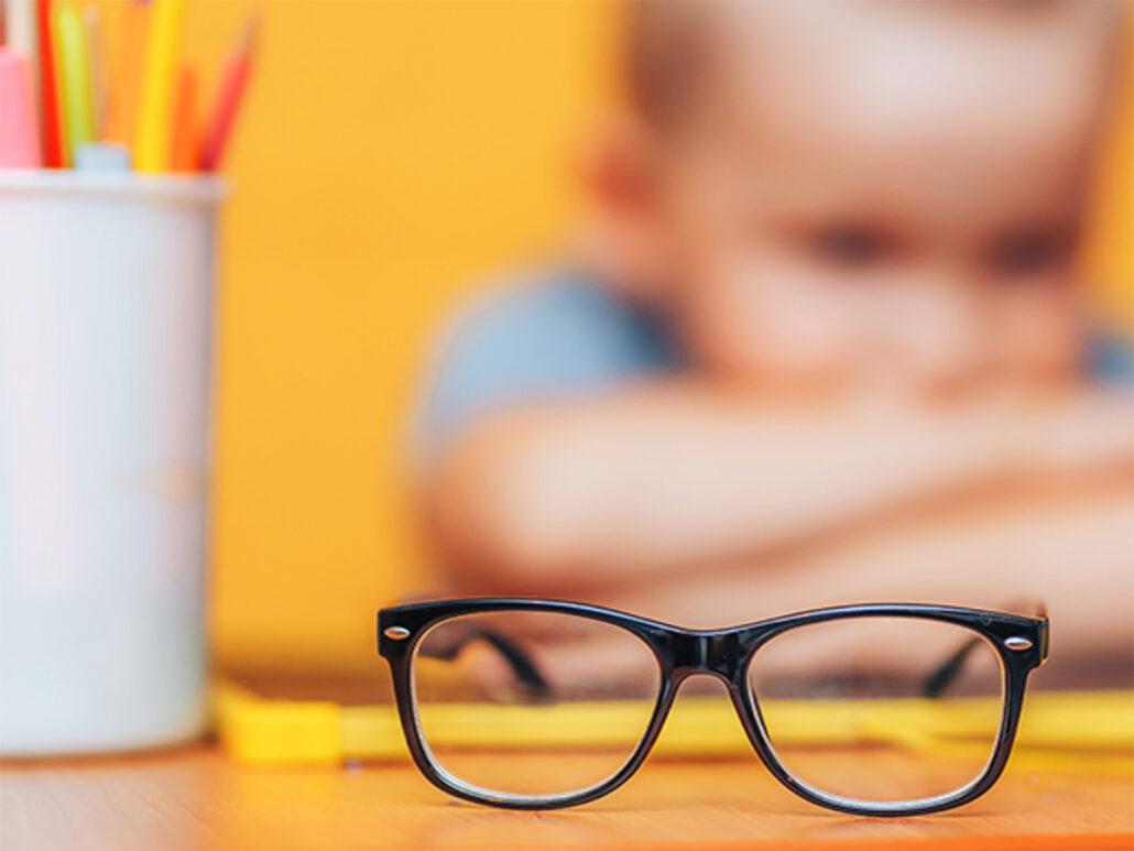 concept image of myopia with a boy furthest from the viewer unfocussed, and glasses closest to the view in focus